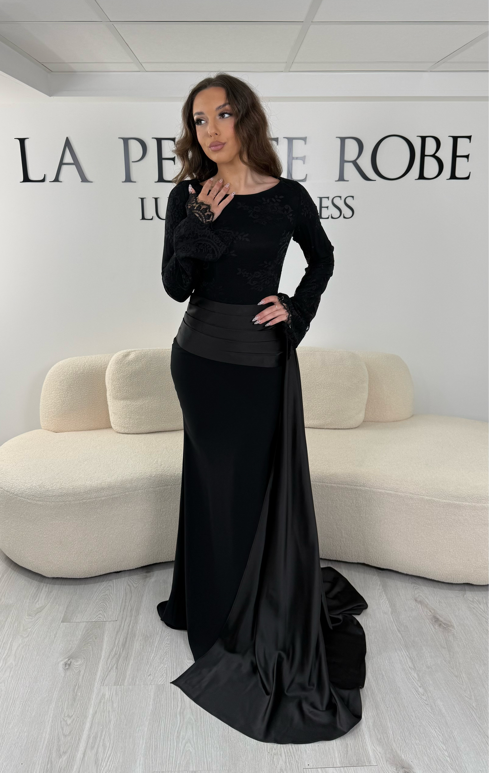 Découvrez cette robe de soirée noire avec col bateau, manches longues et élégante traîne sur le côté. Une robe sans fente, parfaite pour une allure raffinée et sophistiquée.