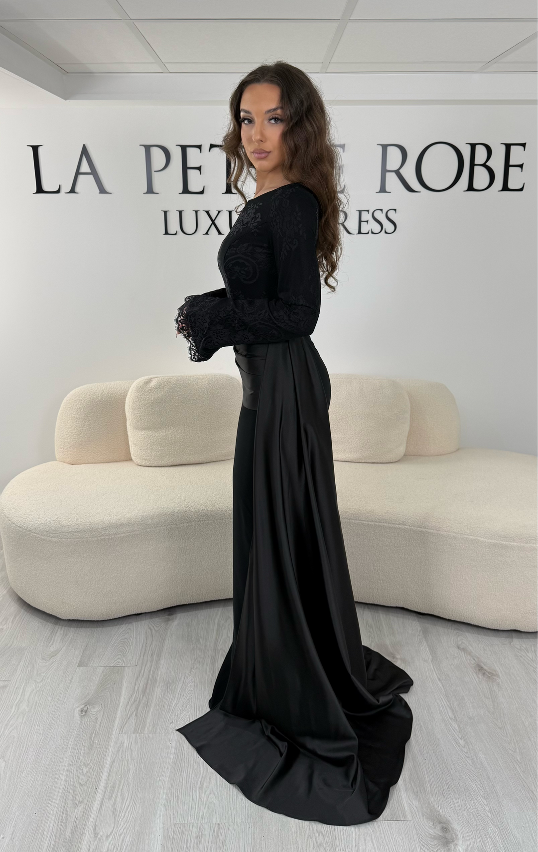 Découvrez cette robe de soirée noire avec col bateau, manches longues et élégante traîne sur le côté. Une robe sans fente, parfaite pour une allure raffinée et sophistiquée.