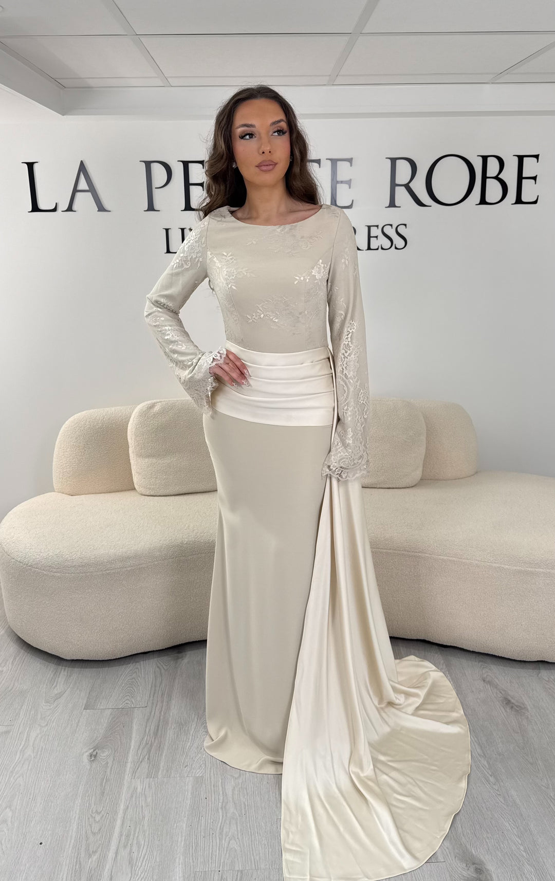 Découvrez cette robe de soirée beige avec col rond, manches longues en dentelle et élégante traîne sur le côté. Une robe sans fente, parfaite pour une allure raffinée.