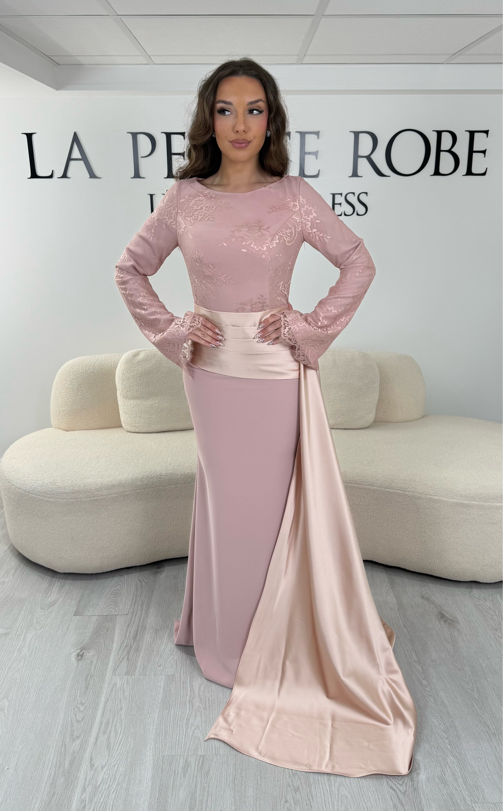 Découvrez cette robe de soirée rose avec col rond, manches longues en dentelle et élégante traîne sur le côté. Une robe sans fente, parfaite pour une allure raffinée.