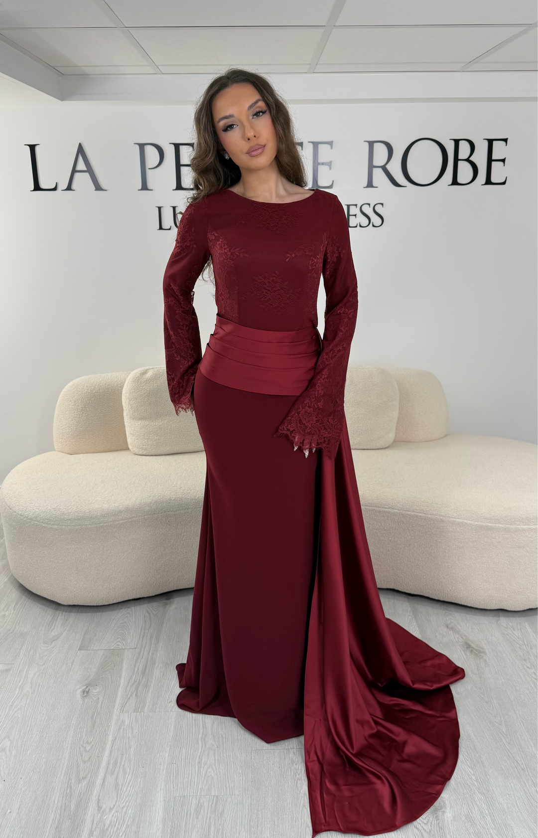 Découvrez cette robe de soirée bordeaux avec col rond, manches longues en dentelle et élégante traîne sur le côté. Une robe sans fente, parfaite pour une allure raffinée.