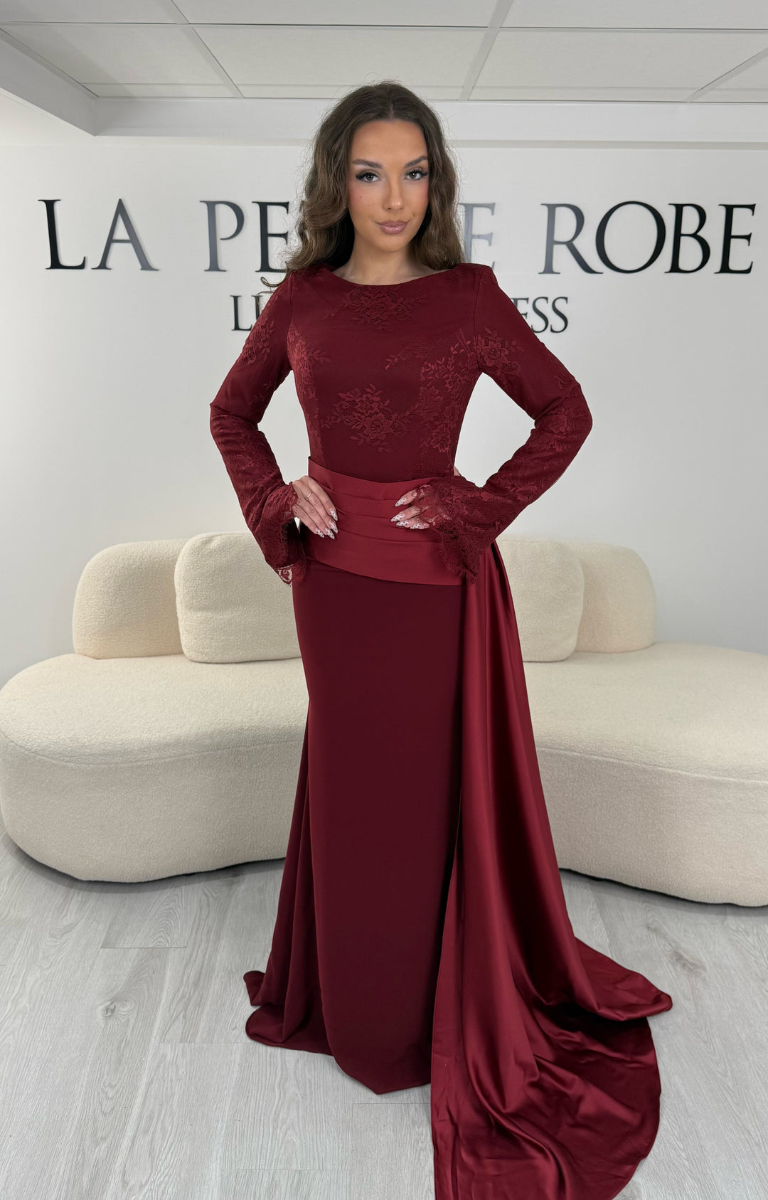 Découvrez cette robe de soirée bordeaux avec col rond, manches longues en dentelle et élégante traîne sur le côté. Une robe sans fente, parfaite pour une allure raffinée.