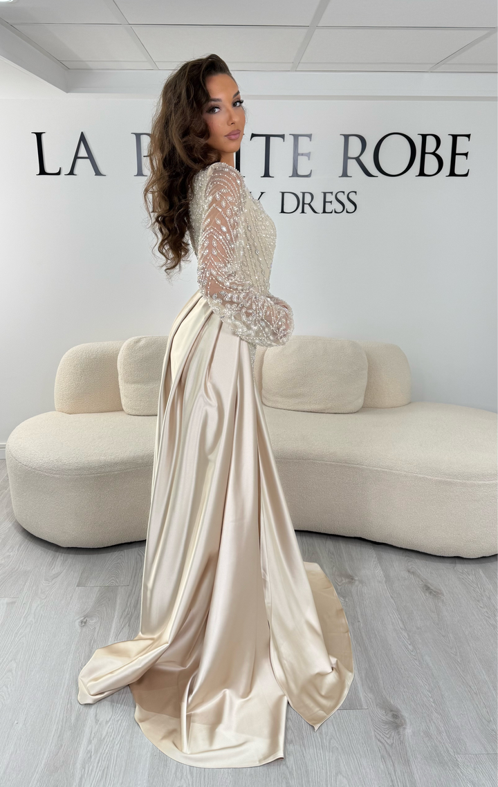 Découvrez cette robe de soirée beige avec col carré, manches longues brodées et traîne amovible. Une robe élégante sans fente, parfaite pour vos plus belles occasions.