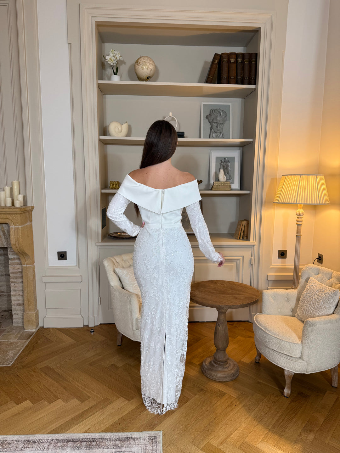 Robe de cérémonie blanche élégante avec col bateau, manches longues et fente à l’arrière. Une robe raffinée pour vos événements.