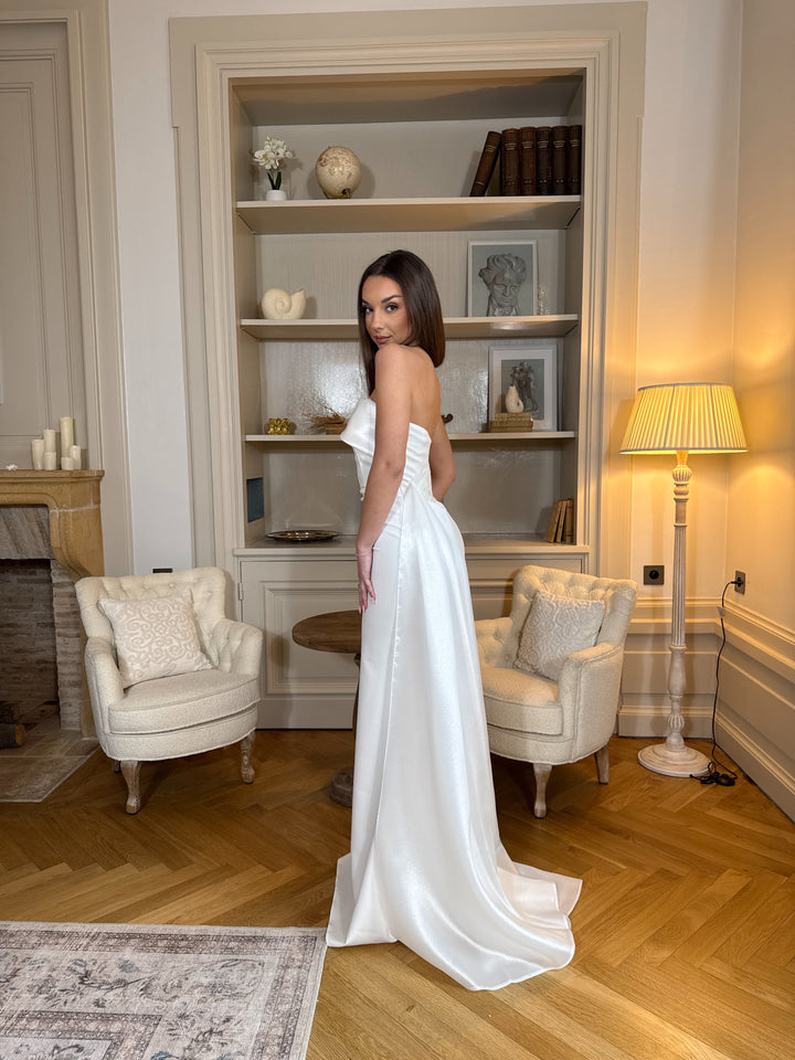 Longue robe de mariée blanche élégante, col bustier sans manches, coupe fluide sans fente. Une robe raffinée pour un mariage chic et intemporel.