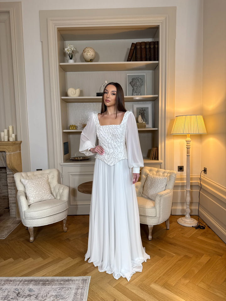 Longue robe de mariée blanche élégante à manches longues, col carré et coupe fluide sans fente. Une robe raffinée pour un mariage chic.