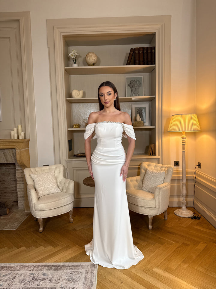 Robe de mariée blanche élégante au col bateau, coupe fluide sans fente. Une robe raffinée et intemporelle pour un mariage chic.