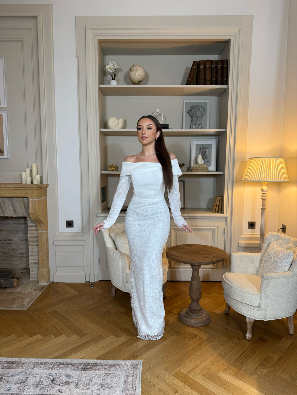 Robe de cérémonie blanche élégante avec col bateau, manches longues et fente à l’arrière. Une robe raffinée pour vos événements.