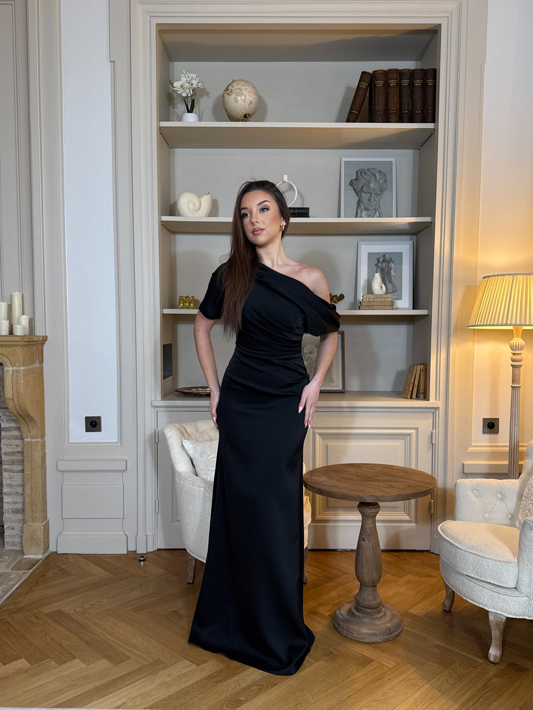 Robe de soirée noire chic au col asymétrique, sans manches et sans fente. Une robe élégante et moderne pour vos soirées raffinées.