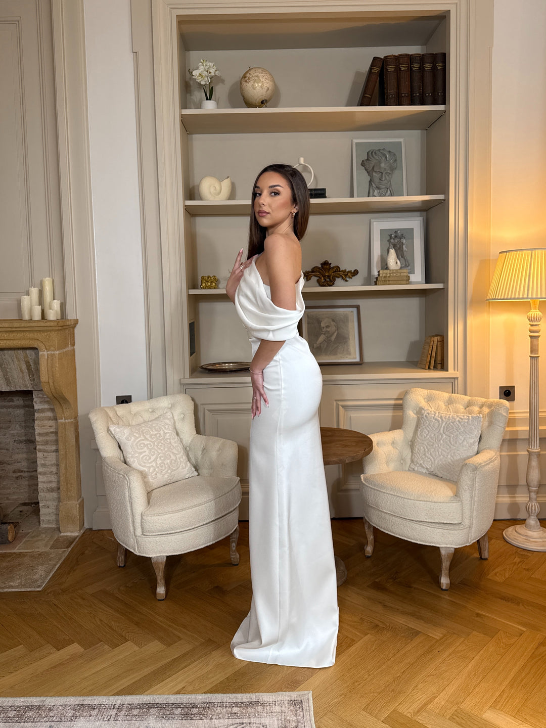 Robe de mariée blanche élégante au col asymétrique, coupe fluide sans fente. Une robe chic et raffinée pour un mariage moderne.