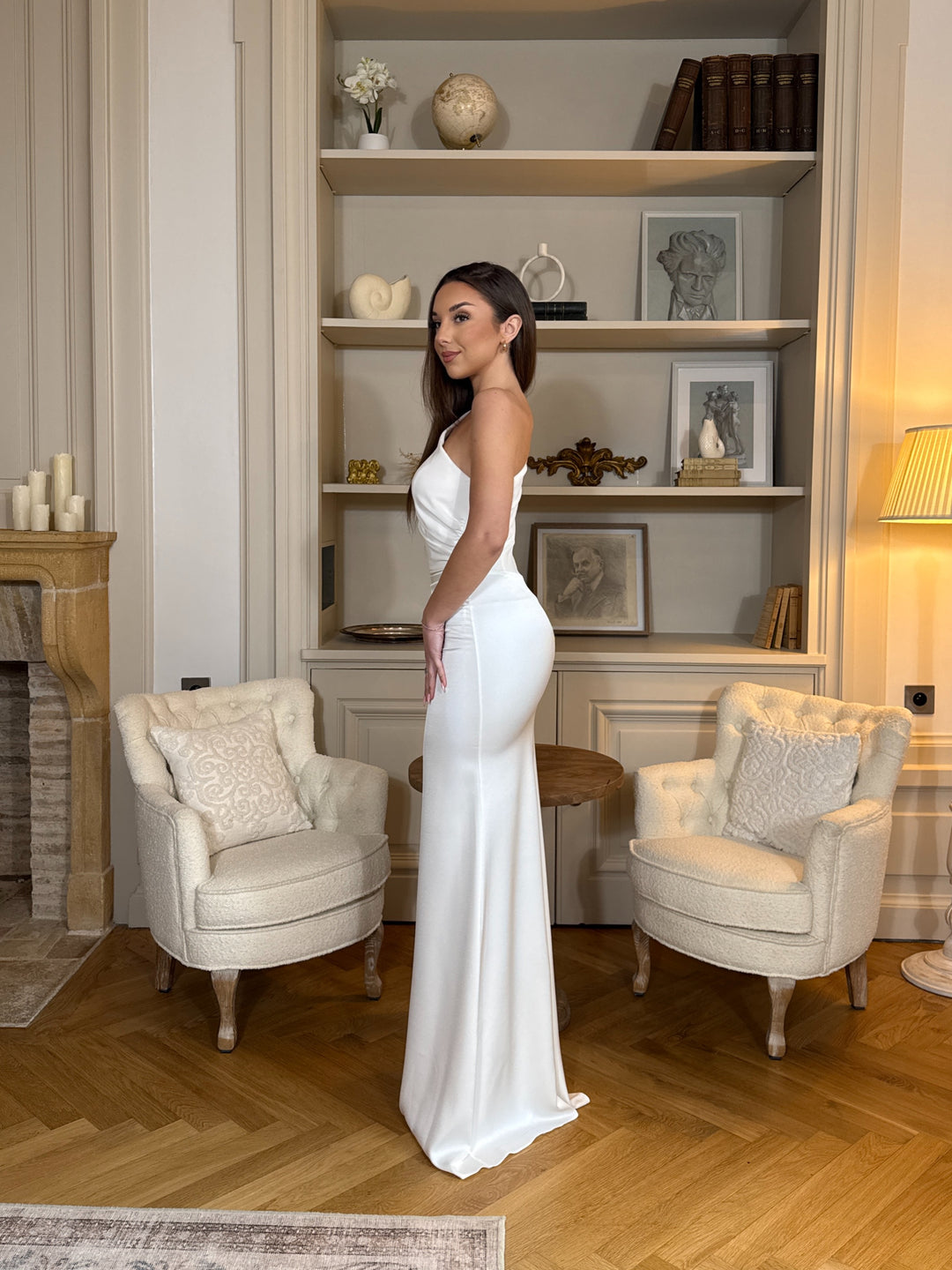 Robe de mariée blanche chic au col asymétrique, sans manches et sans fente. Une robe élégante et moderne pour un mariage raffiné.