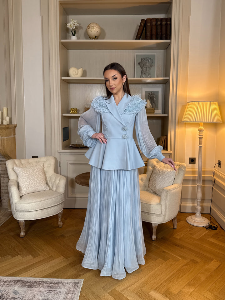 Ensemble blazer avec jupe bleu chic, manches longues plissées et détails floraux. Élégant, fluide et raffiné, parfait pour mariage ou cérémonie.