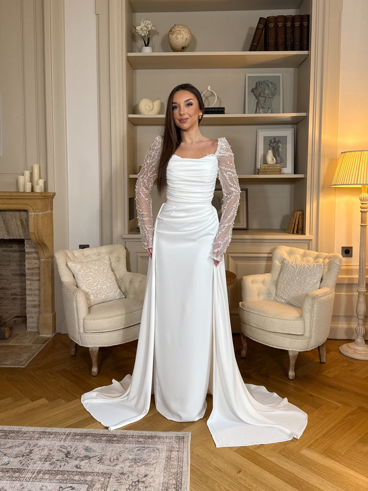 Découvrez une élégante robe de mariée blanc avec manches longues ornées, coupe flatteuse et tissu fluide, parfaite pour sublimer votre cérémonie.