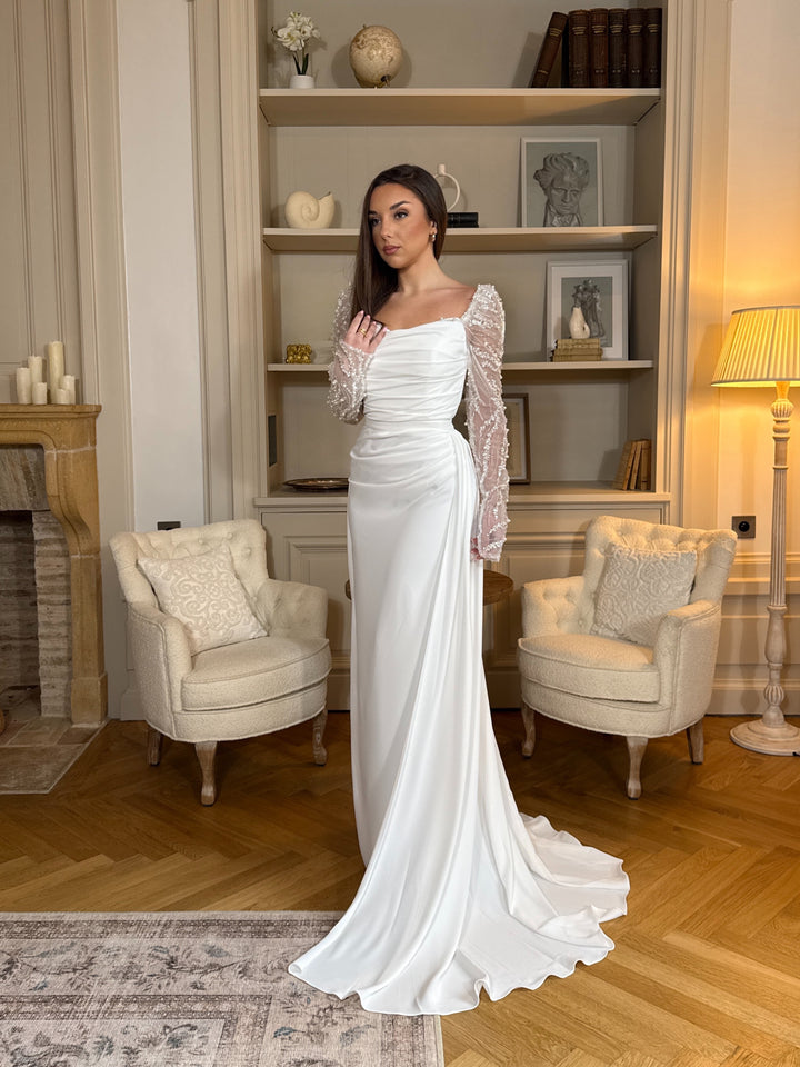 Découvrez une élégante robe de mariée blanc avec manches longues ornées, coupe flatteuse et tissu fluide, parfaite pour sublimer votre cérémonie.
