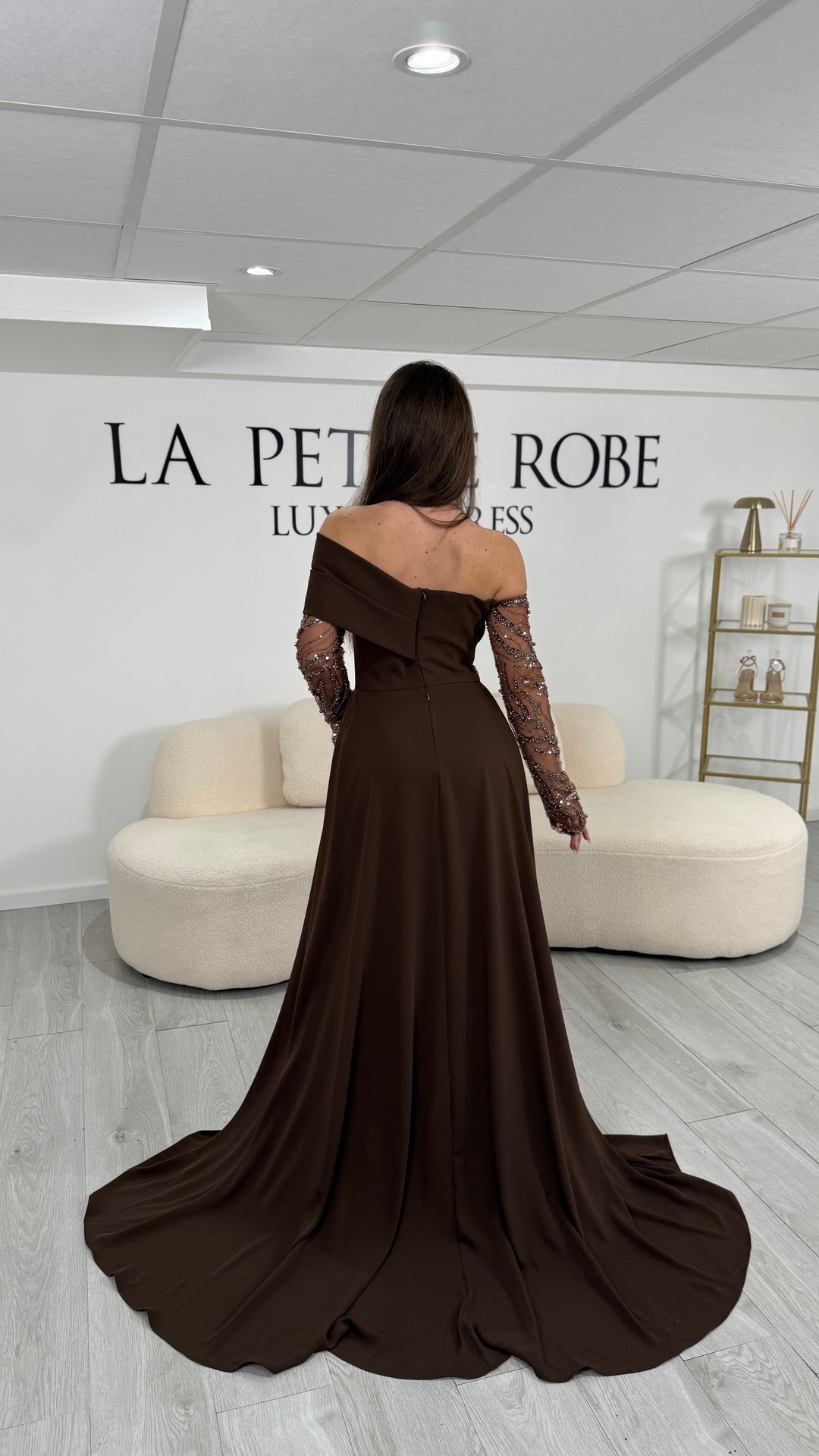 Longue robe de soirée marron élégante au col asymétrique et manches longues. Modèle raffiné avec fente latérale, idéal pour vos soirées chic.