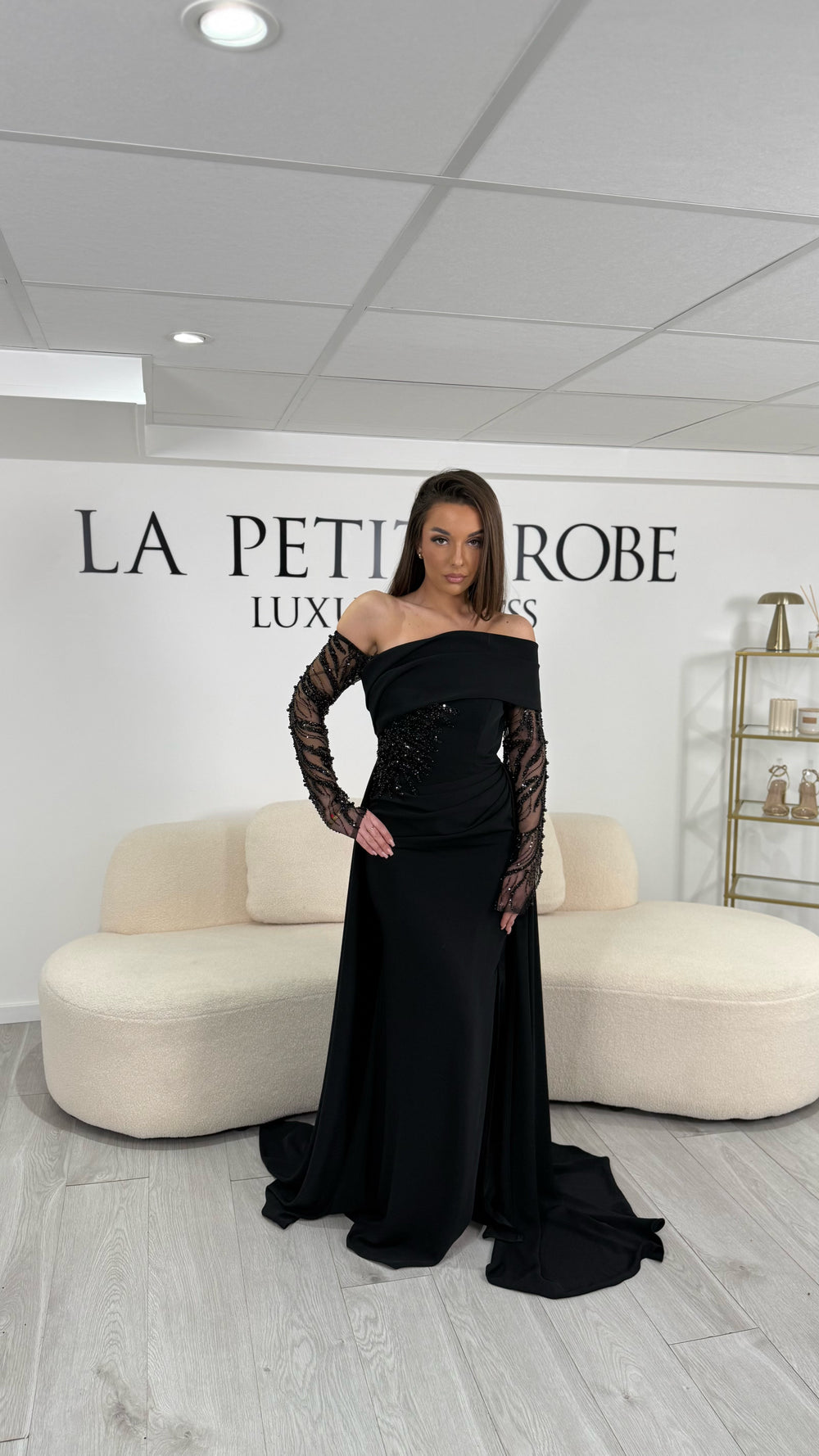 Longue robe de soirée noir chic au col asymétrique et manches longues. Modèle élégant avec fente latérale, parfait pour vos soirées prestigieuses.