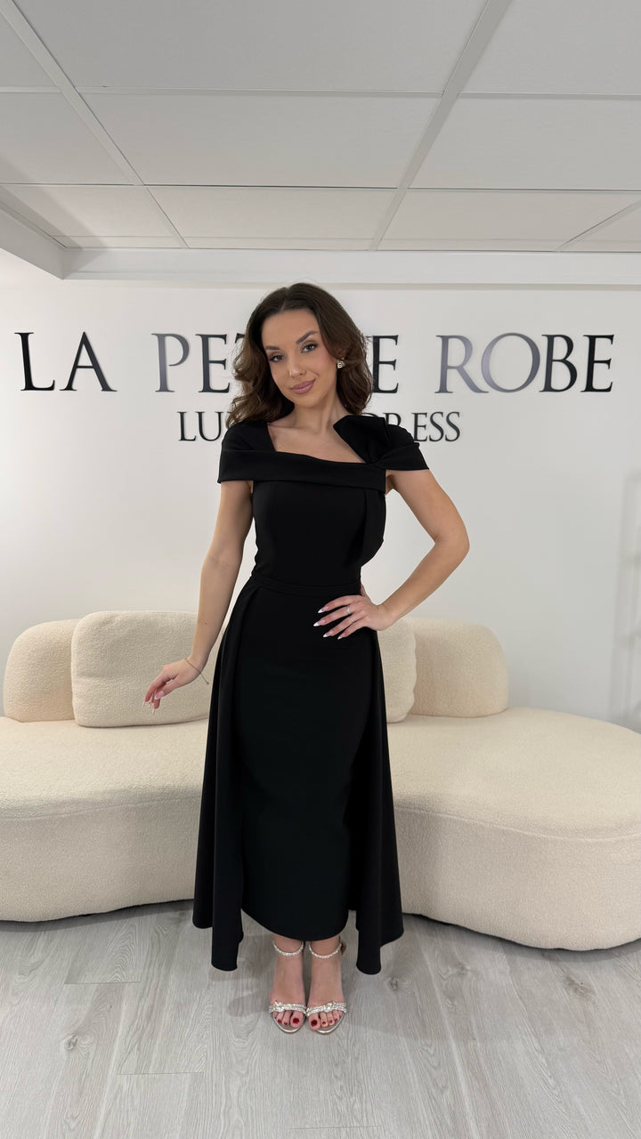 Robe de soirée noire midi avec col bateau élégant et coupe sans manche. Sans fente, silhouette raffinée idéale pour réception et soirée chic.