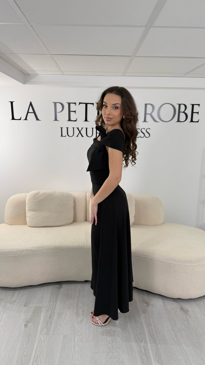 Robe de soirée noire midi avec col bateau élégant et coupe sans manche. Sans fente, silhouette raffinée idéale pour réception et soirée chic.