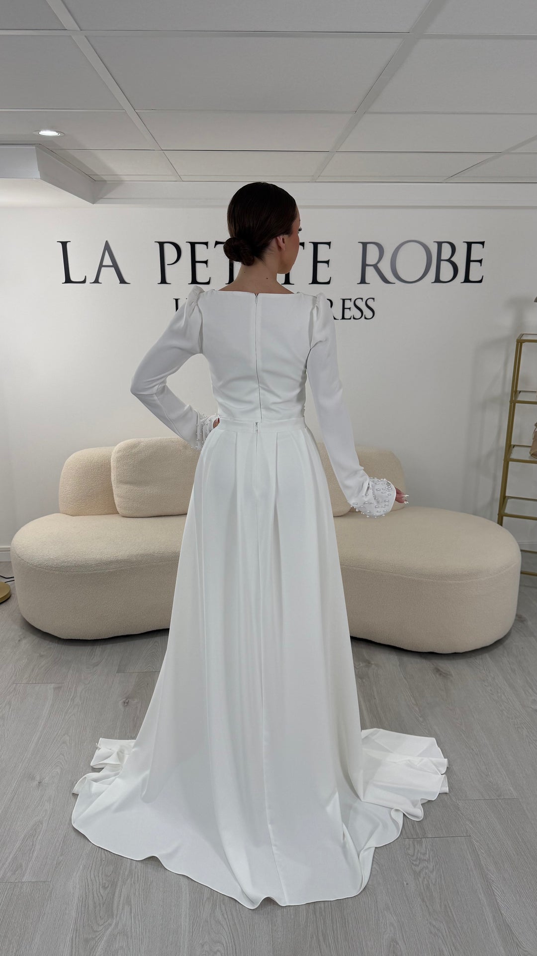 Robe de mariée blanche élégante avec col rond et manches longues. Robe longue sans fente, coupe raffinée et détails perlés, parfaite pour une cérémonie de mariage chic.