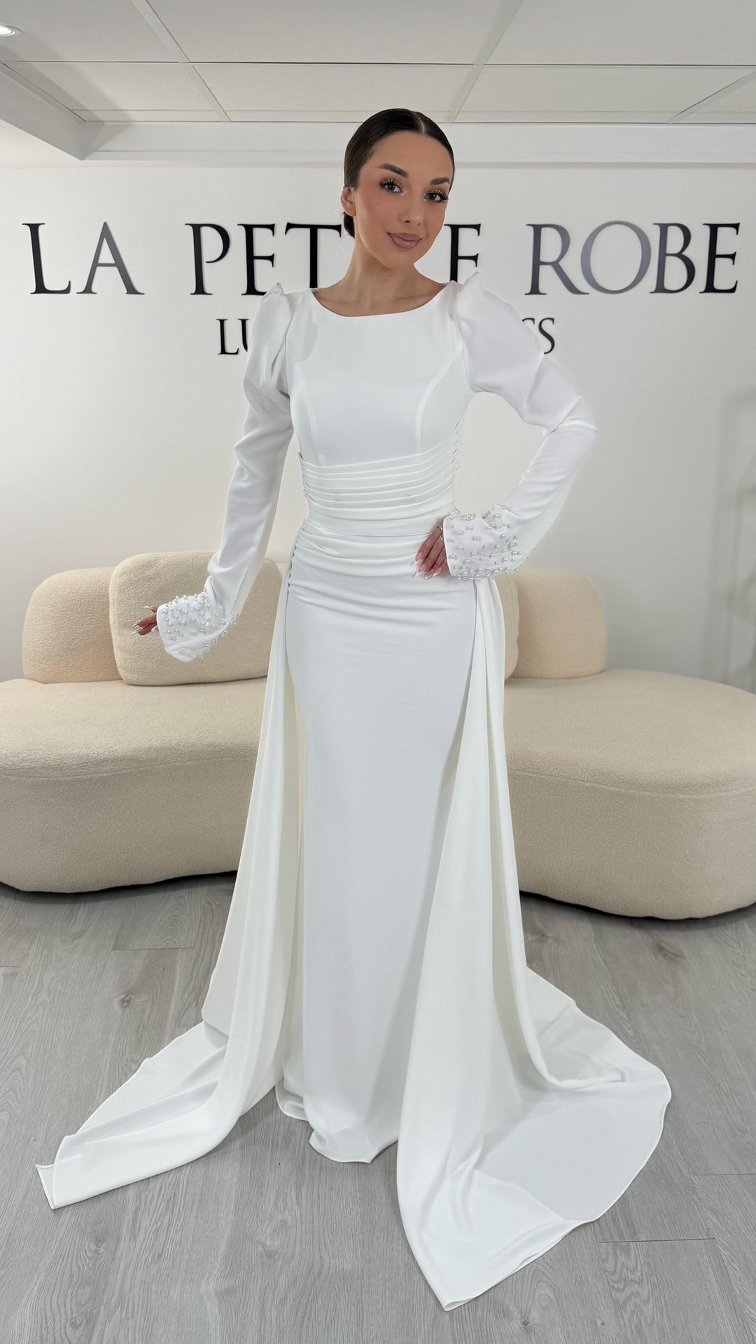 Robe de mariée blanche élégante avec col rond et manches longues. Robe longue sans fente, coupe raffinée et détails perlés, parfaite pour une cérémonie de mariage chic.