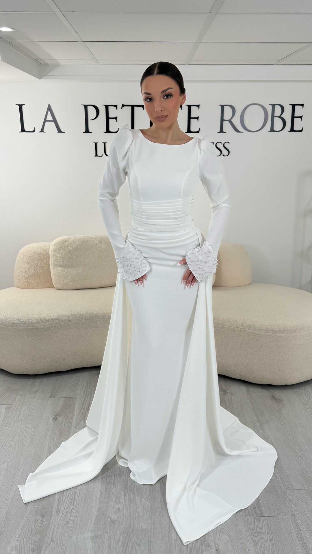 Robe de mariée blanche élégante avec col rond et manches longues. Robe longue sans fente, coupe raffinée et détails perlés, parfaite pour une cérémonie de mariage chic.