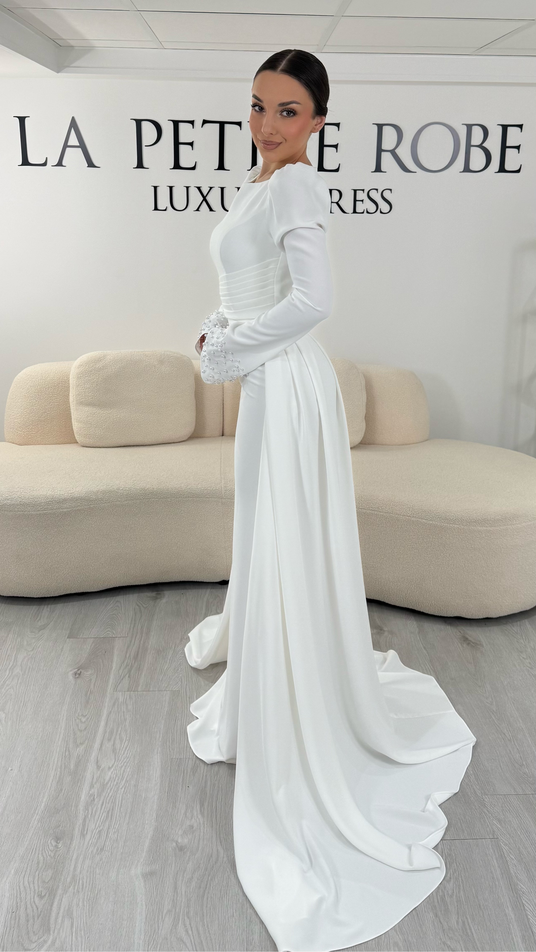 Robe de mariée blanche élégante avec col rond et manches longues. Robe longue sans fente, coupe raffinée et détails perlés, parfaite pour une cérémonie de mariage chic.