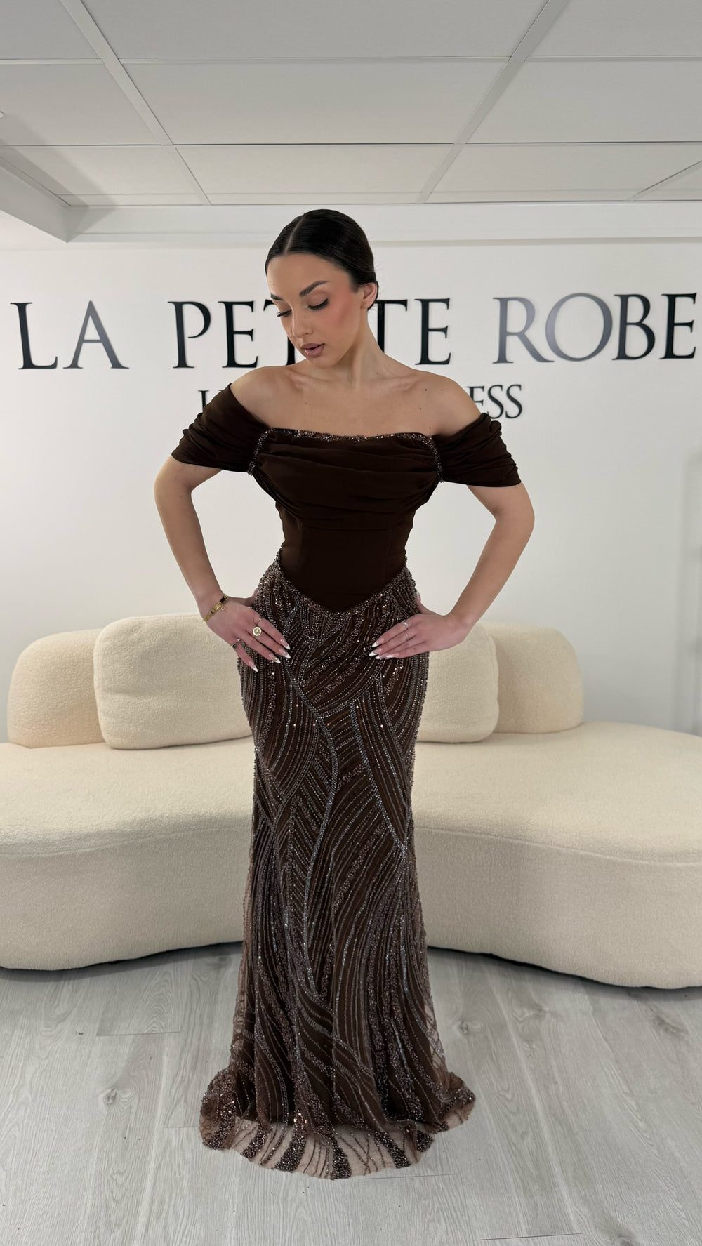Robe de soirée marron élégante sans manches avec col bardot et jupe scintillante. Robe longue sans fente idéale pour soirée chic.