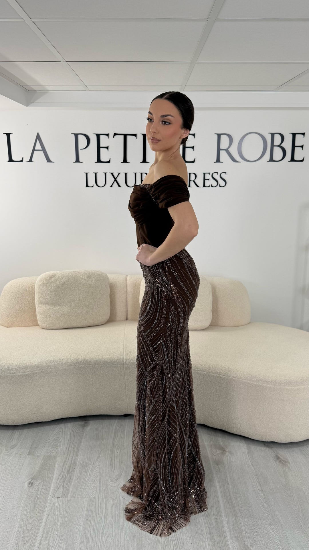 Robe de soirée marron élégante sans manches avec col bardot et jupe scintillante. Robe longue sans fente idéale pour soirée chic.