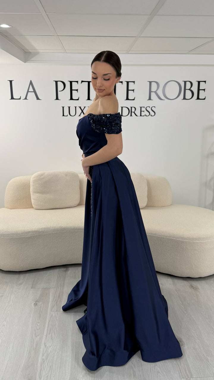 Robe de soirée bleu marine élégante sans manches avec col bardot et sequins. Robe longue sans fente idéale pour soirée chic.