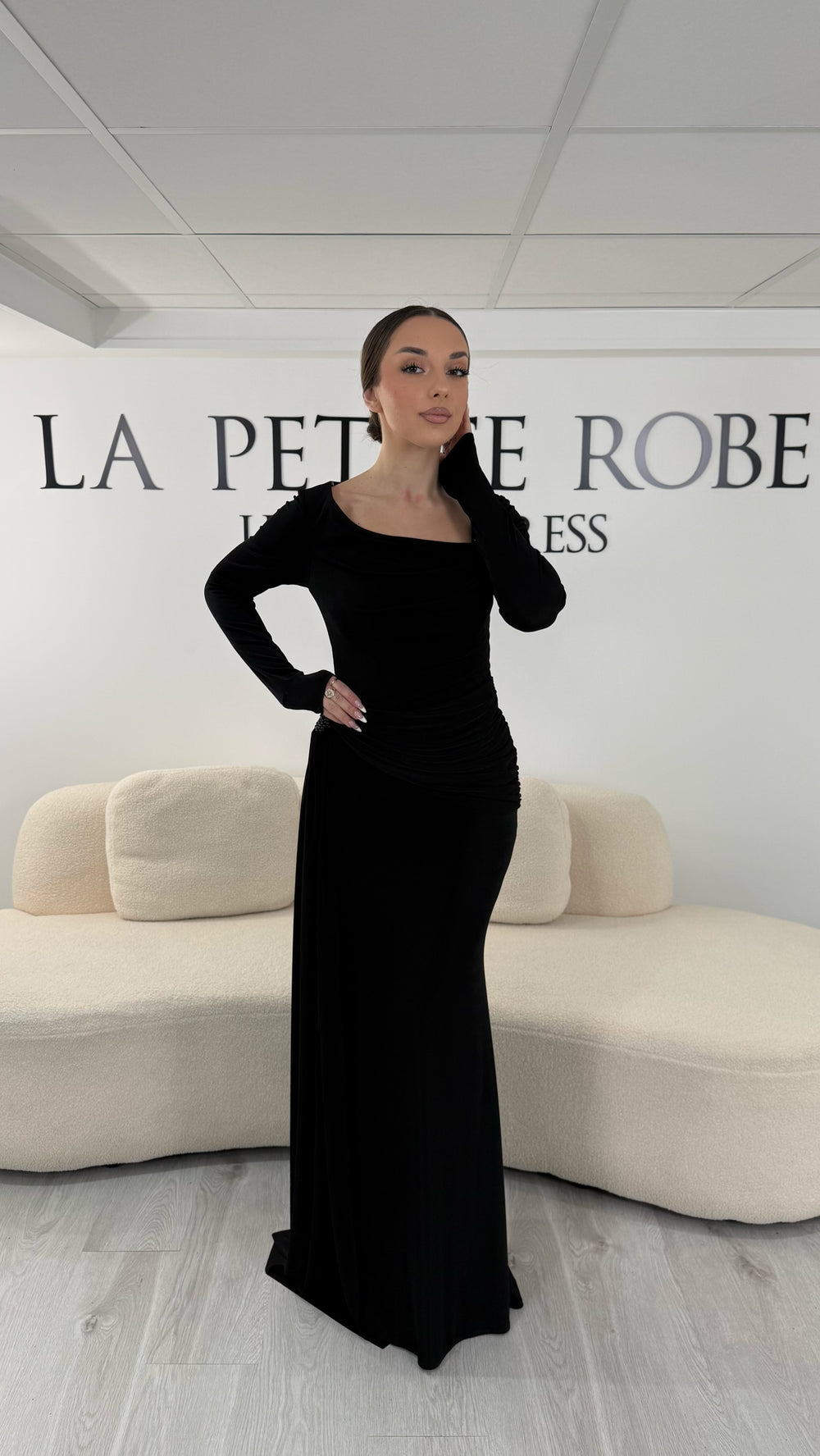 Robe de soirée noire élégante avec col bateau drapé et manches longues. Robe longue sans fente idéale pour soirée chic.