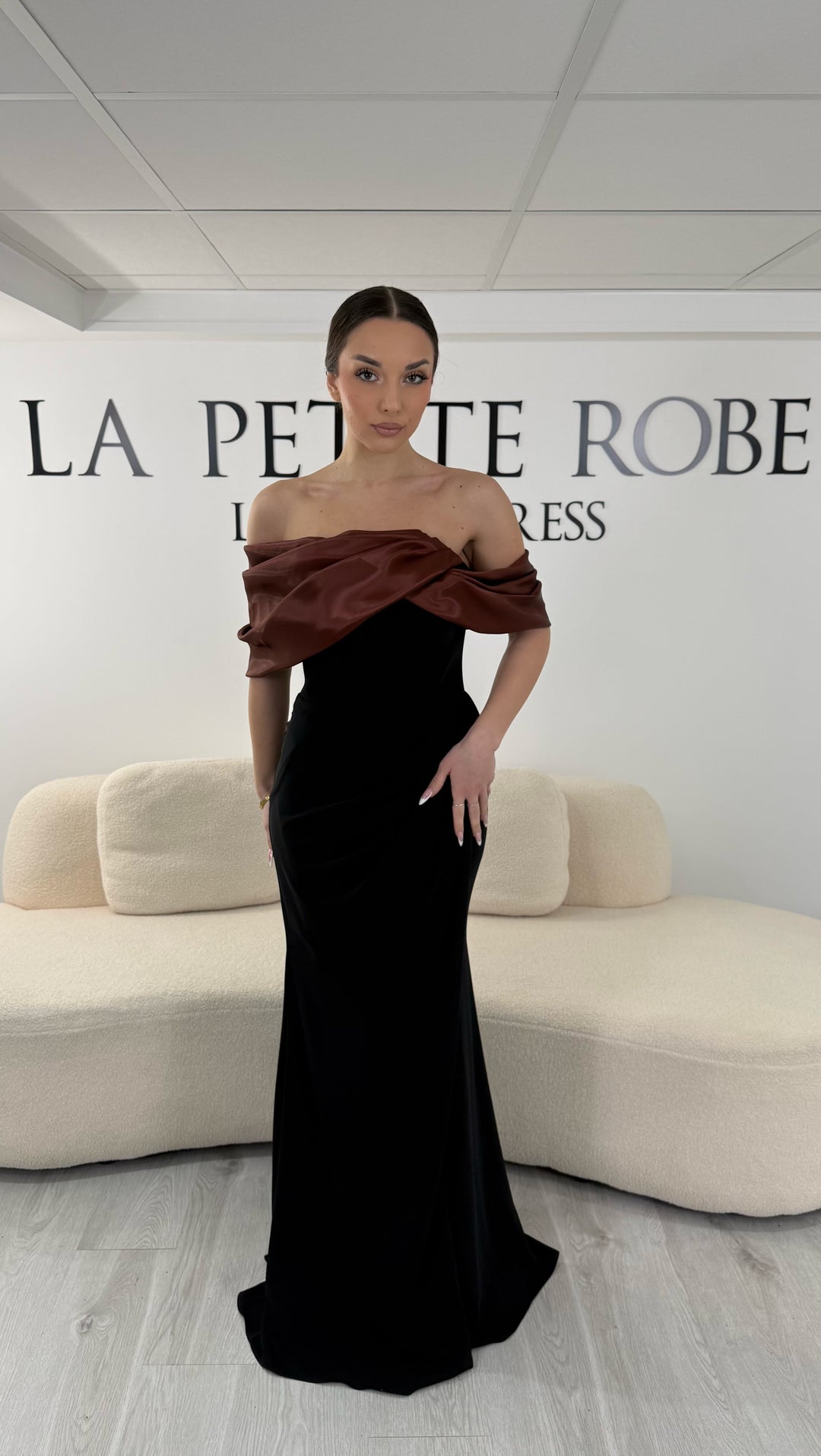 Robe de soirée marron élégante avec col bardot drapé satiné. Robe longue sans manches et sans fente idéale pour soirée chic.