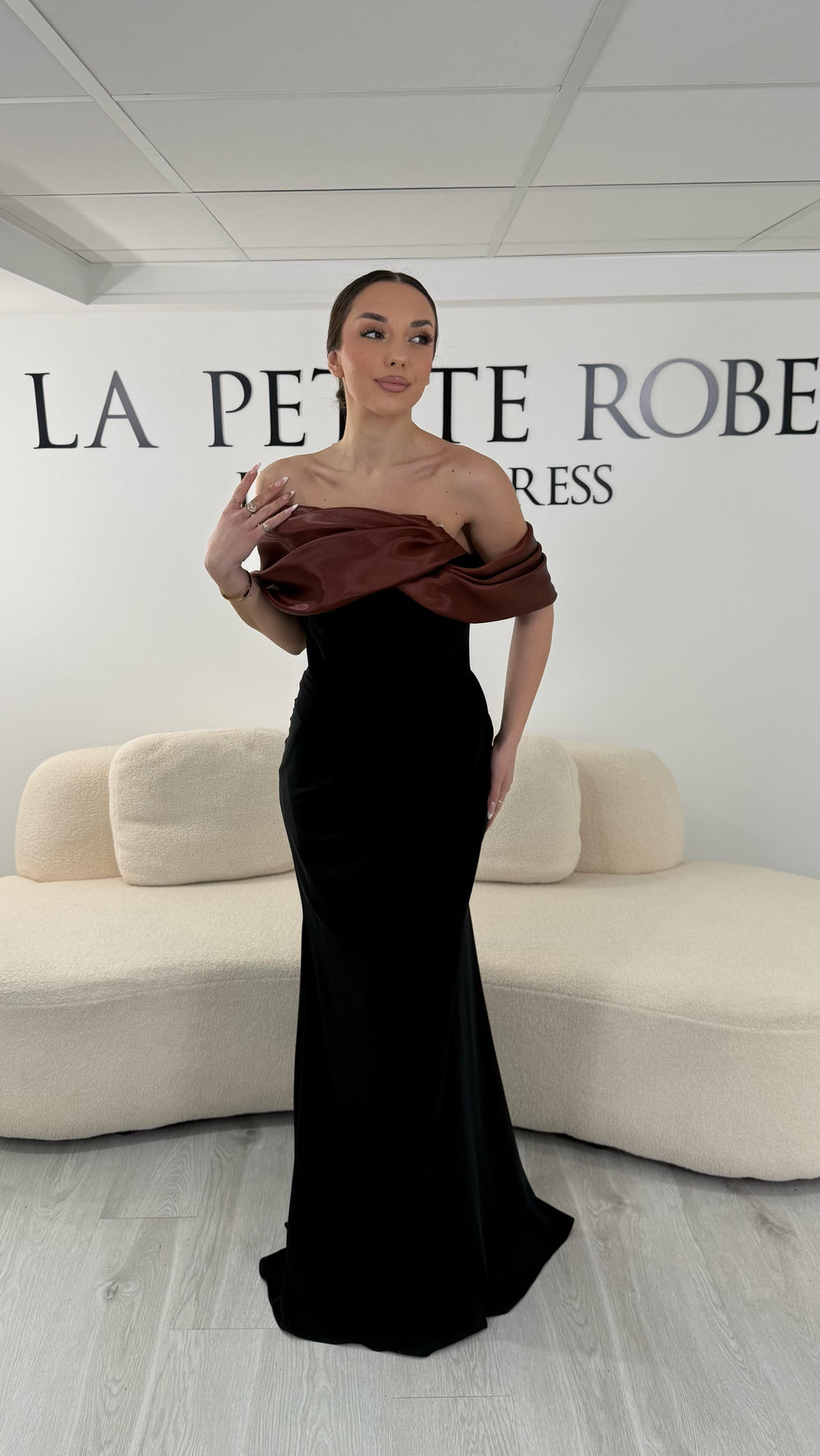 Robe de soirée marron élégante avec col bardot drapé satiné. Robe longue sans manches et sans fente idéale pour soirée chic.