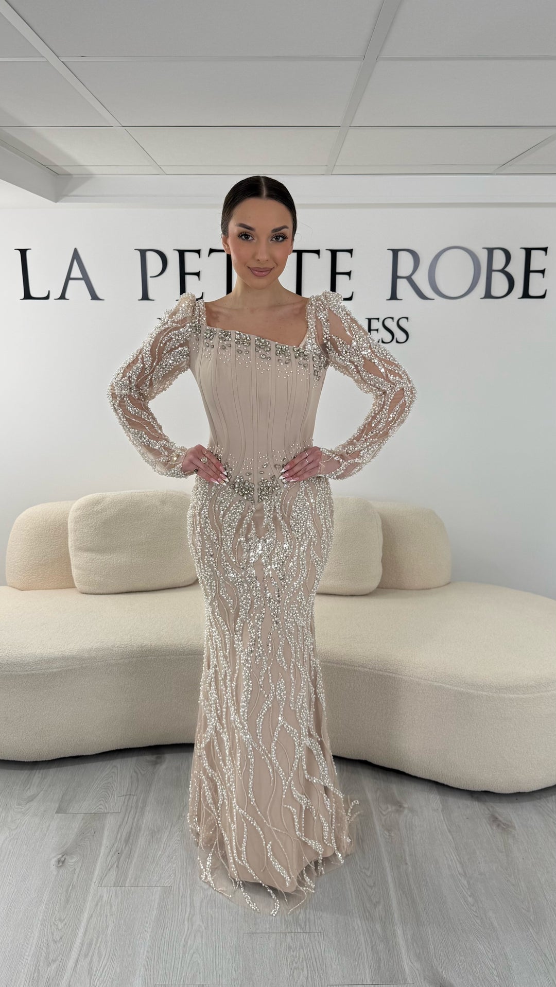 Robe de soirée beige élégante avec col asymétrique et manches longues brodées. Robe longue sans fente idéale pour gala ou soirée chic.