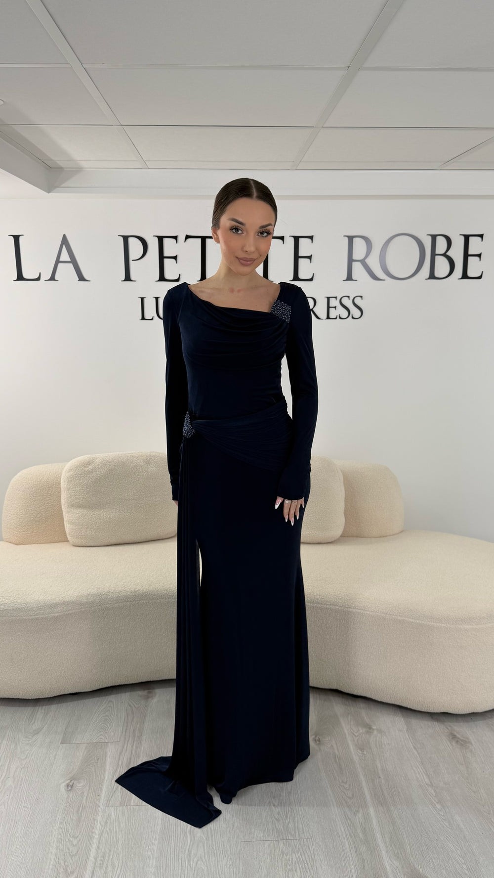 Robe de soirée bleu marine élégante avec col bateau drapé et manches longues. Robe longue sans fente idéale pour soirée chic.