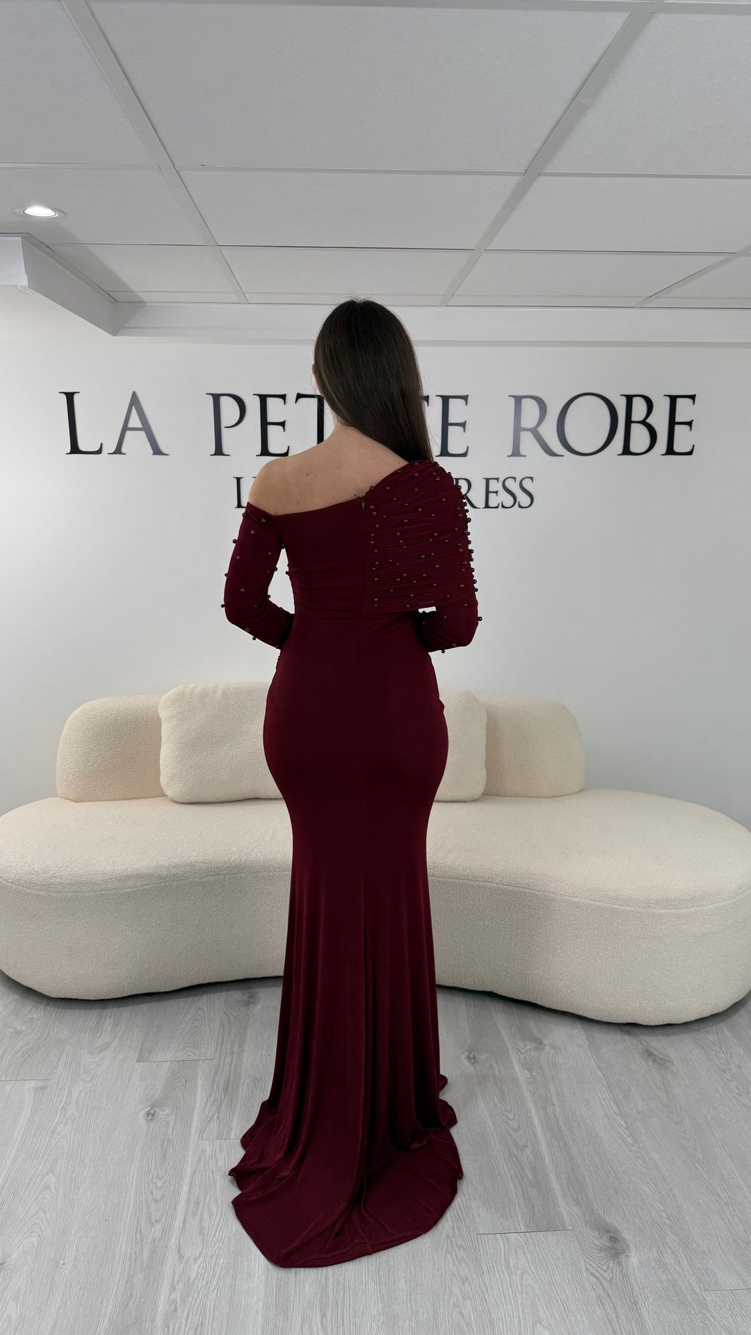 Robe de soirée bordeaux longue, sans fente, avec col asymétrique et manches longues. Élégante avec détails perlés pour vos soirées.