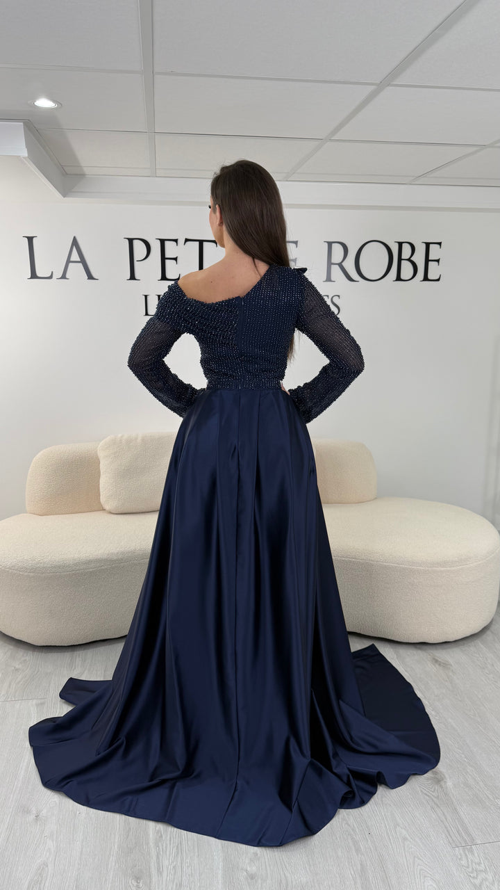 Robe de soirée bleu marine longue, sans fente, avec col asymétrique, manches longues et surjupe amovible. Élégante et modulable.