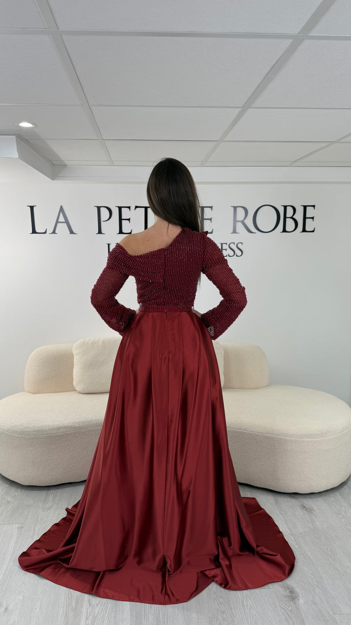 Robe de soirée bordeaux longue, sans fente, avec col asymétrique, manches longues et surjupe amovible. Élégante et modulable.