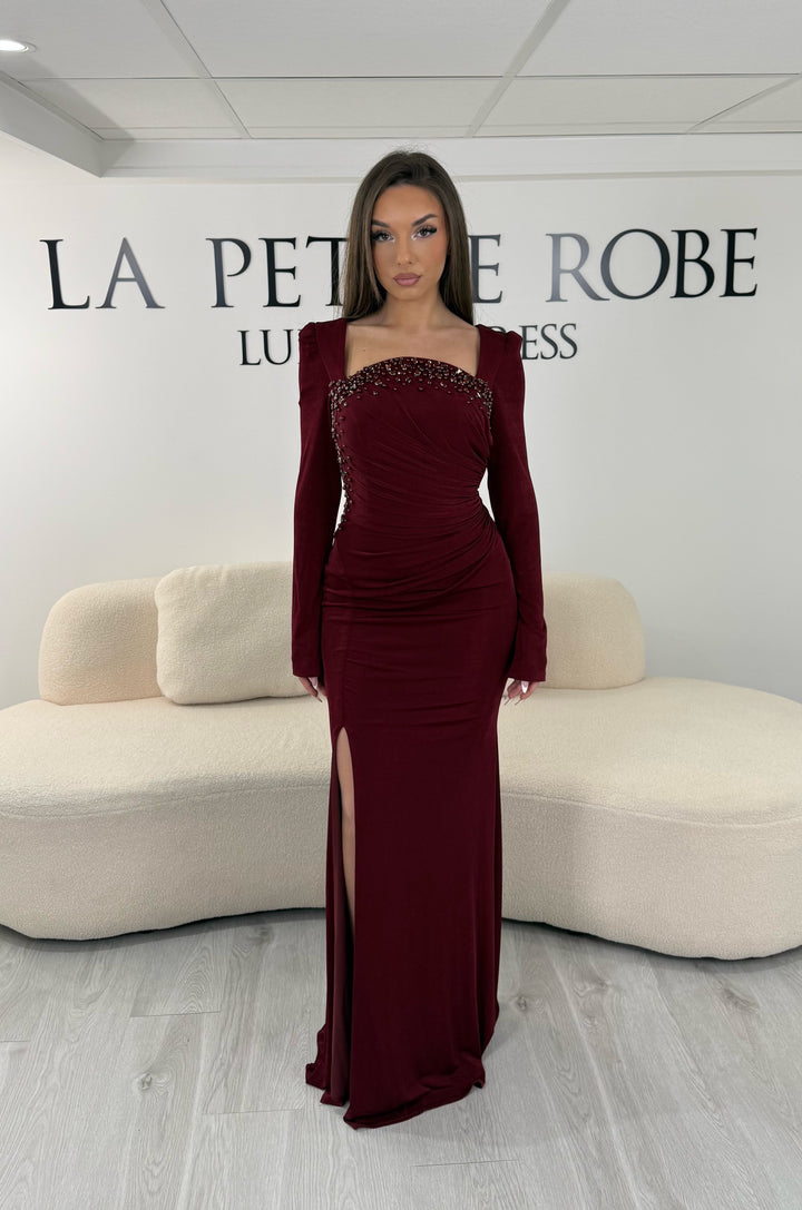 Robe de soirée bordeaux longue avec fente, col droit et manches longues. Élégante avec détails perlés pour vos soirées chic.