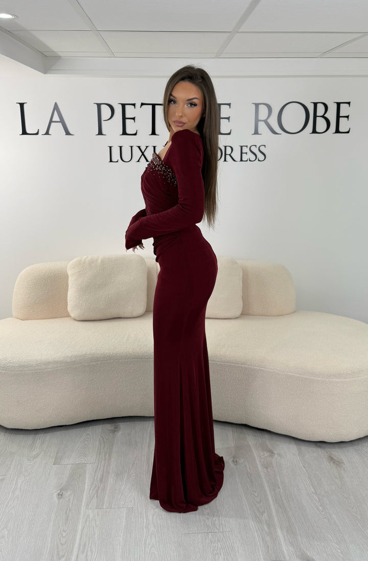 Robe de soirée bordeaux longue avec fente, col droit et manches longues. Élégante avec détails perlés pour vos soirées chic.