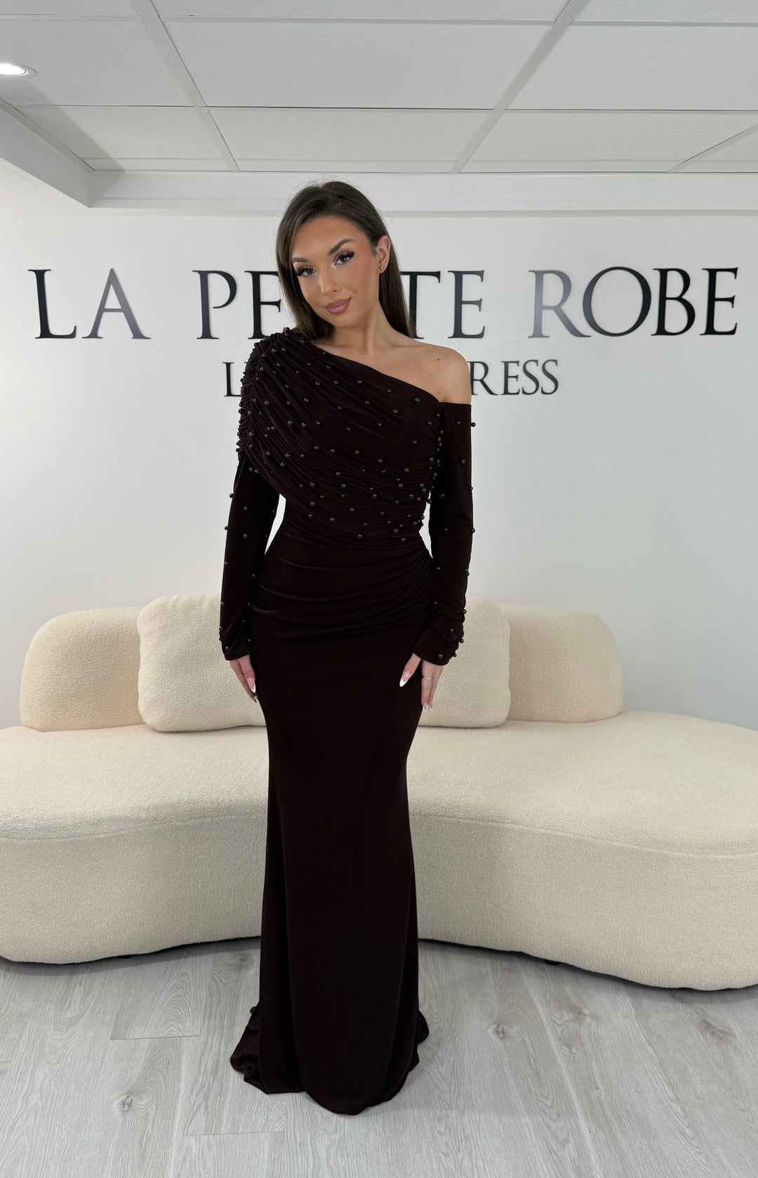 Robe de soirée marron longue, sans fente, avec col asymétrique et manches longues. Élégante avec détails perlés pour vos soirées.