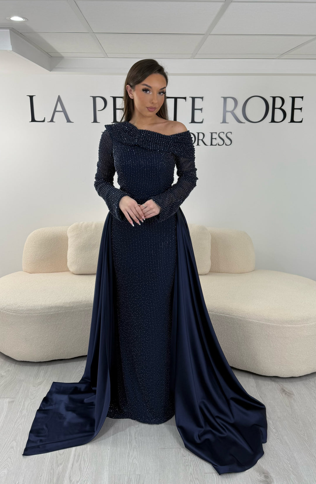 Robe de soirée bleu marine longue, sans fente, avec col asymétrique, manches longues et surjupe amovible. Élégante et modulable.