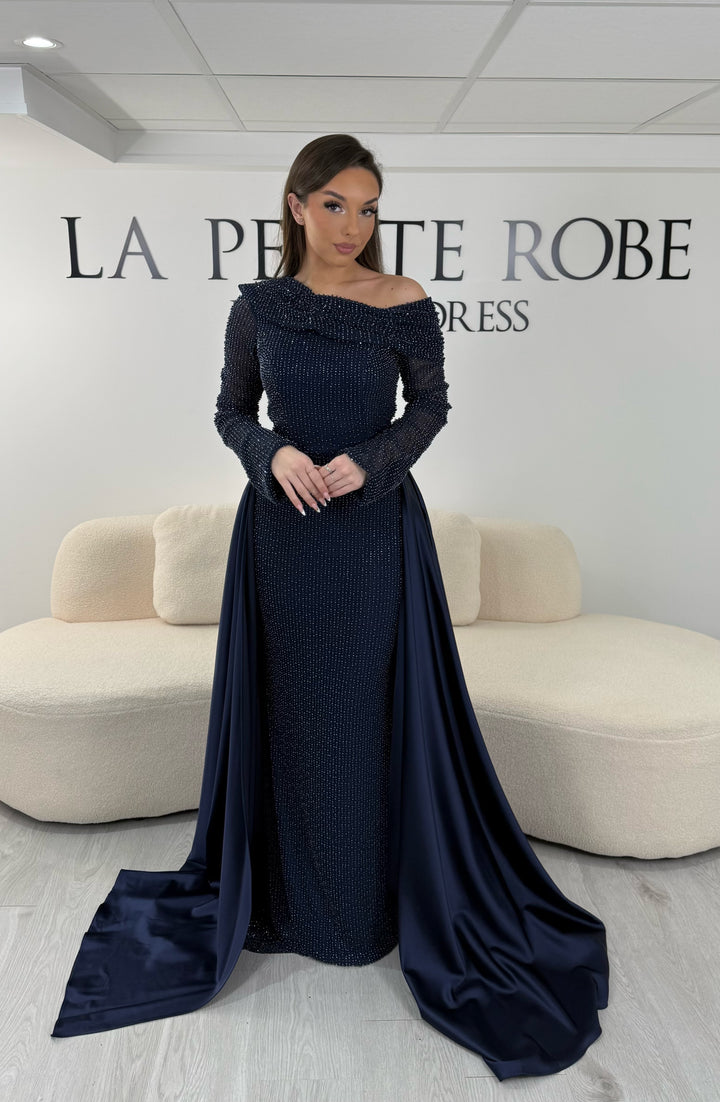 Robe de soirée bleu marine longue, sans fente, avec col asymétrique, manches longues et surjupe amovible. Élégante et modulable.