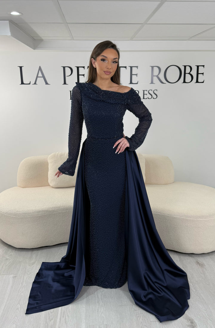 Robe de soirée bleu marine longue, sans fente, avec col asymétrique, manches longues et surjupe amovible. Élégante et modulable.