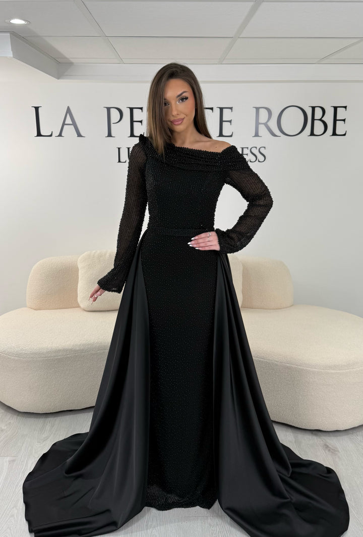 Robe de soirée noire longue, sans fente, avec col asymétrique, manches longues et surjupe amovible. Élégante et modulable.