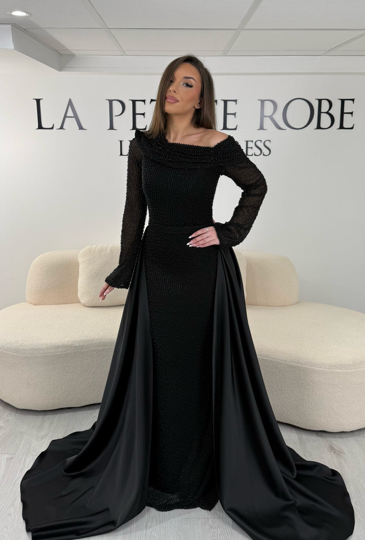 Robe de soirée noire longue, sans fente, avec col asymétrique, manches longues et surjupe amovible. Élégante et modulable.
