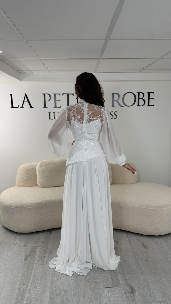 Robe de mariée blanche longue avec décolleté bustier sous col montant en dentelle et boléro amovible. Élégante, sans fente, idéale mariage 2026.