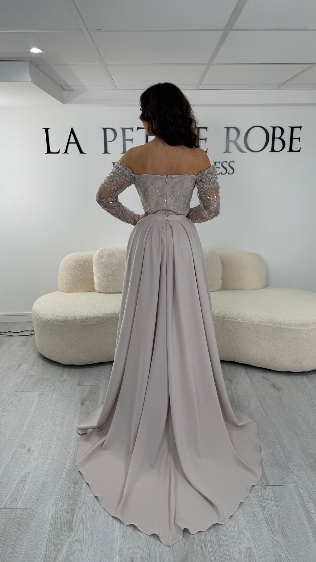 Robe de soirée beige longue avec dentelle, décolleté épaules dénudées et traîne amovible. Élégante, sans fente, idéale mariage 2026.