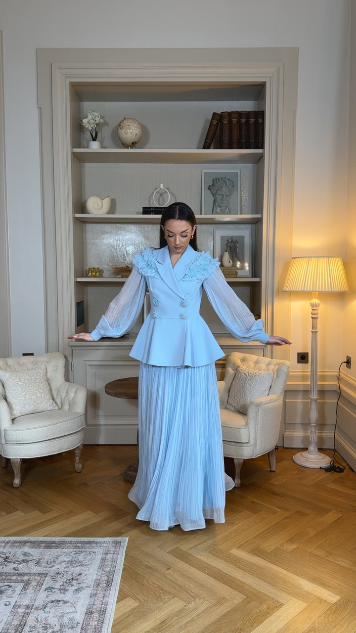 Ensemble blazer avec jupe bleu chic, manches longues plissées et détails floraux. Élégant, fluide et raffiné, parfait pour mariage ou cérémonie.
