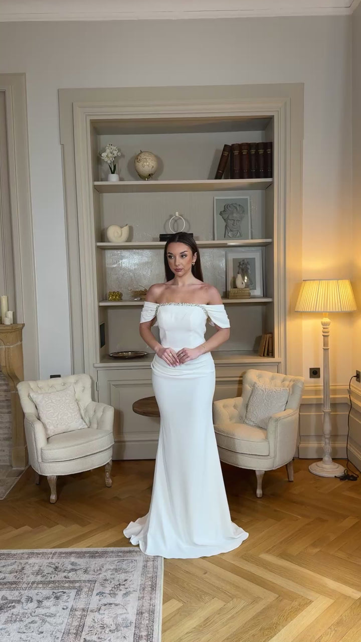 Robe de mariée blanche élégante au col bateau, coupe fluide sans fente. Une robe raffinée et intemporelle pour un mariage chic.