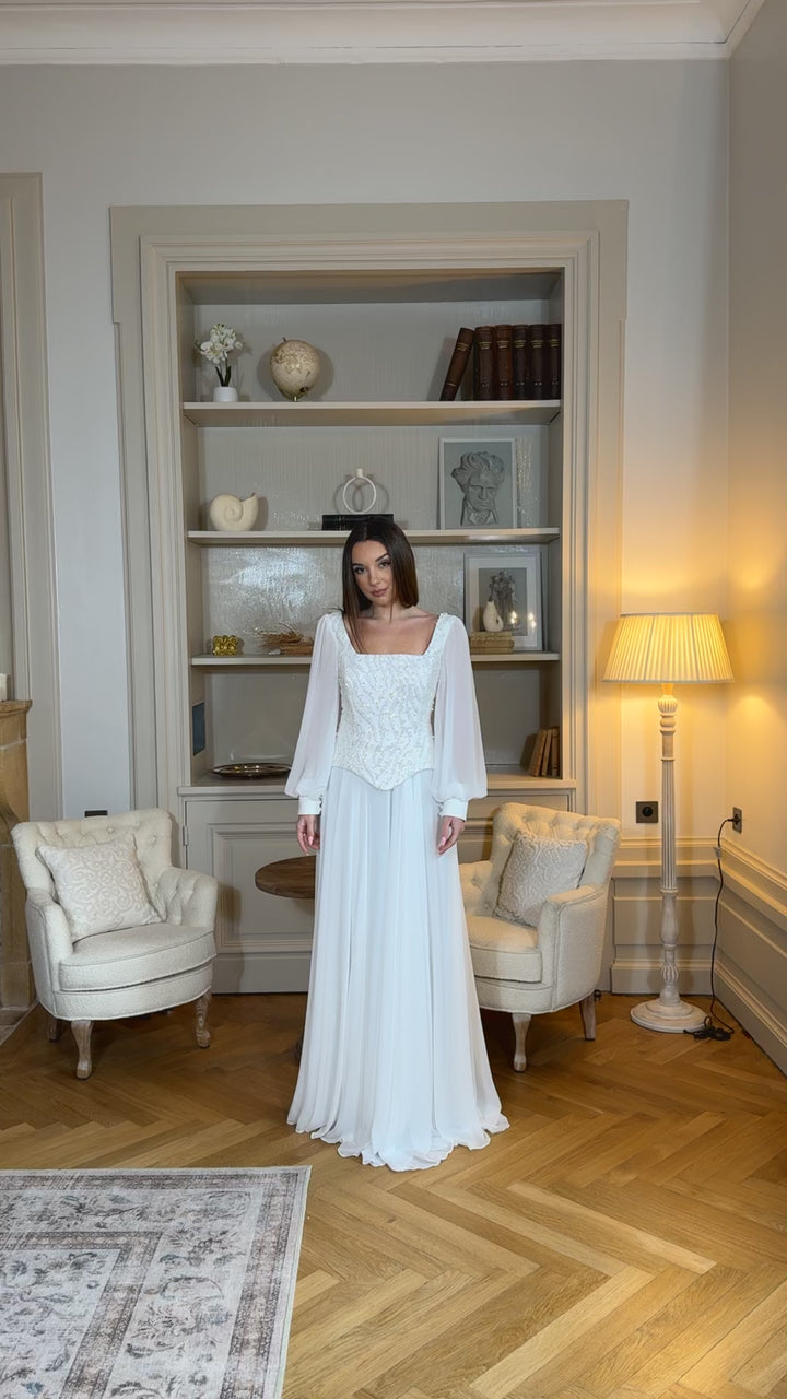 Longue robe de mariée blanche élégante à manches longues, col carré et coupe fluide sans fente. Une robe raffinée pour un mariage chic.